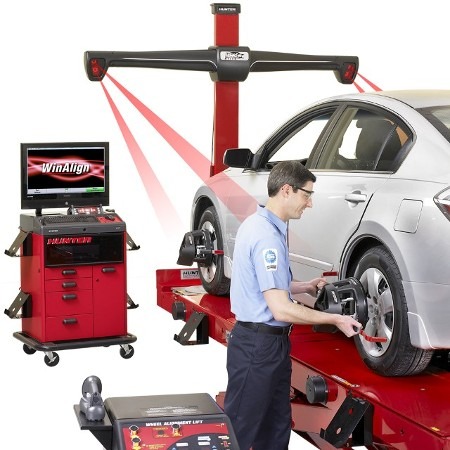 A man is inspecting a car elevated on a lift in a garage, focused on maintenance tasks